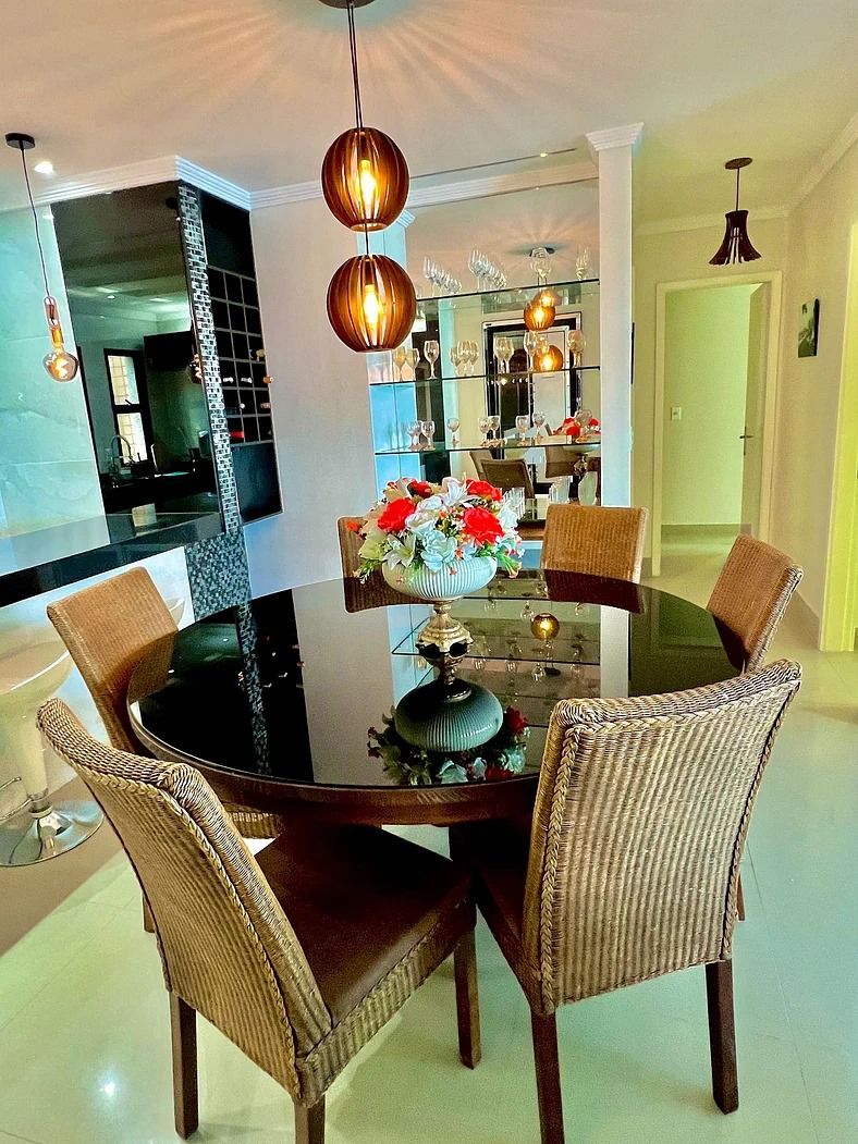 Comedor con una mesa redonda de vidrio, sillas de mimbre y un centro de mesa decorativo.