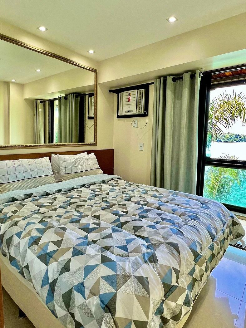 Una habitación de hotel moderna con una cama grande, un espejo, una ventana con cortinas y vistas a zonas verdes.