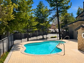 A swimming pool with a curved design, surrounded by a fence and trees. - Shores Lakefront Condo - Lakefront Condo, Walk to Village, Dock, Pool (Big Bear Lake)