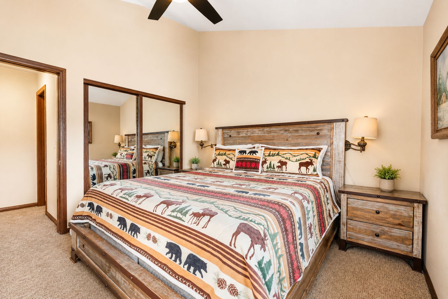 A bedroom with a large bed, a wooden headboard, bedside lamps, a nightstand, a mirror, and a framed picture on the wall.