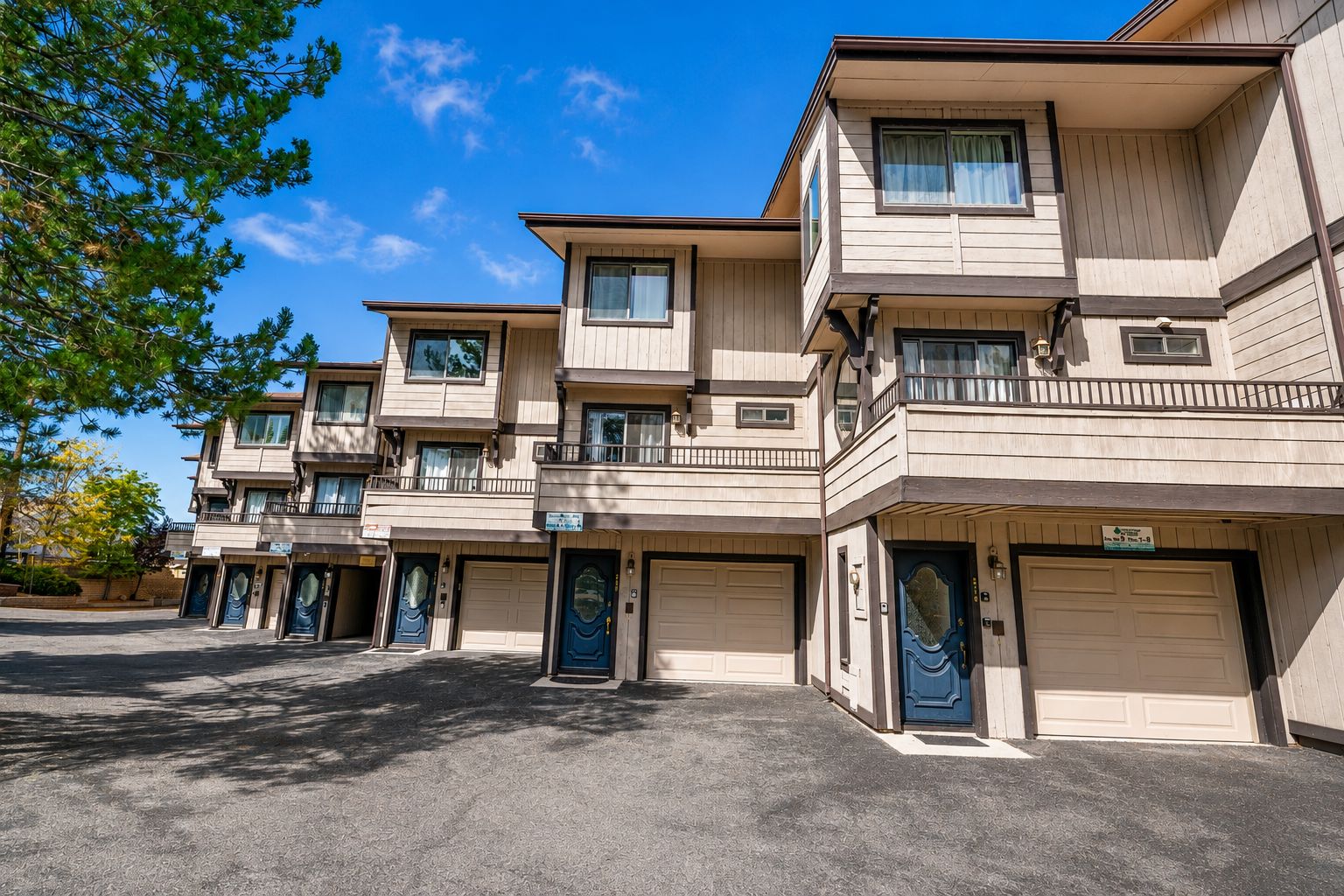 A multi-story residential building with a flat roof, multiple balconies, and a parking area in front.