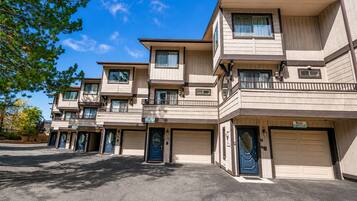 A multi-story residential building with a flat roof, multiple balconies, and a parking area in front.