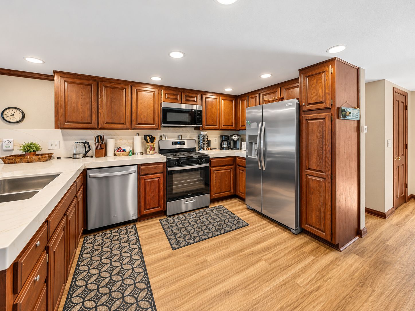 A modern kitchen with wooden cabinets, stainless steel appliances, and a clock on the wall.