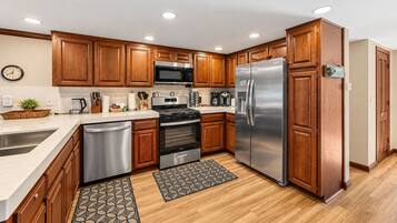 A modern kitchen with wooden cabinets, stainless steel appliances, and a clock on the wall.