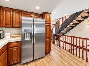 Eine Küche mit Holzausstattung, einem Edelstahlkühlschrank, einem Wasserspender und einer Holztreppe mit Geländer.