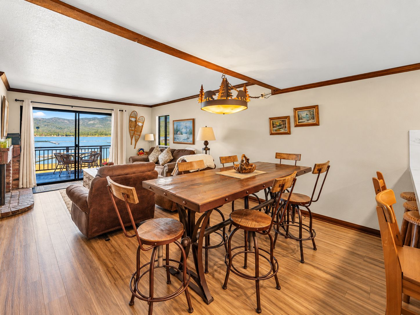 A spacious dining area with a large wooden table and multiple chairs, a sofa, and a view of a lake through a sliding glass door.