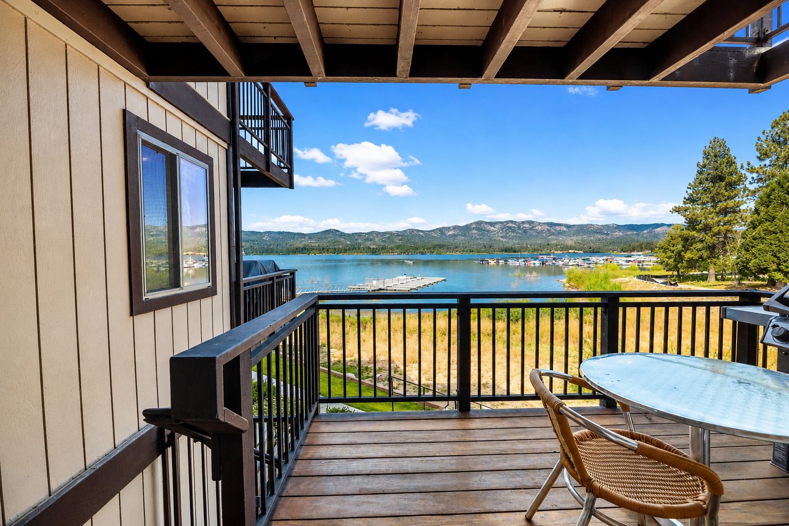 A wooden deck with a table and chairs, overlooking a lake with boats and a dock.