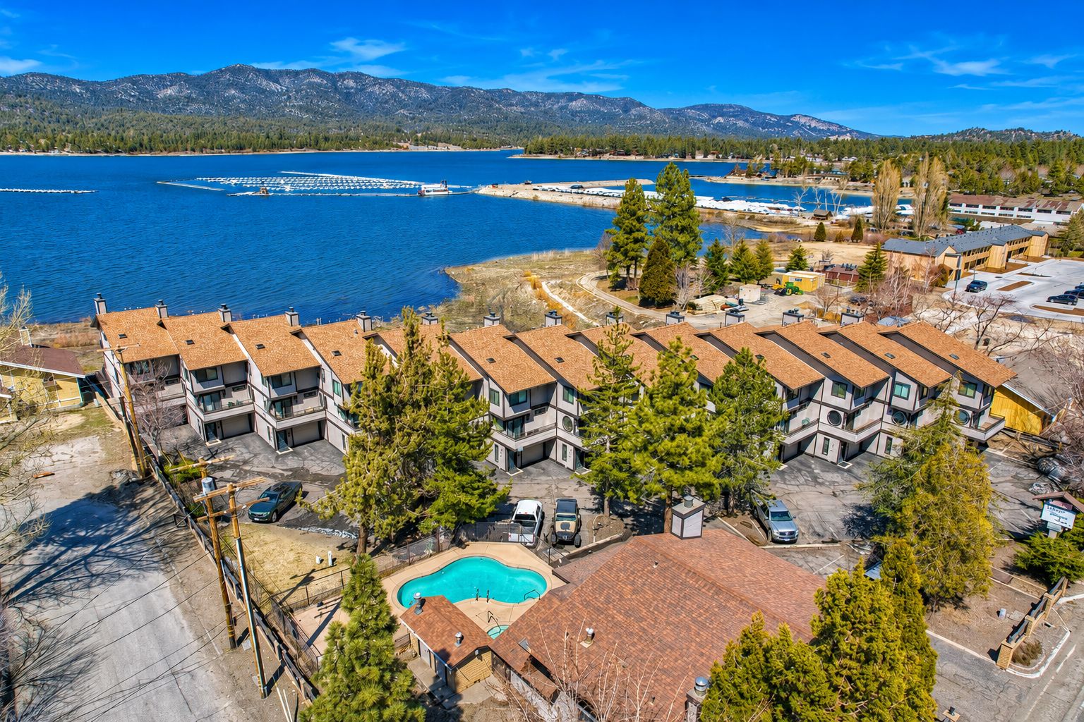 A residential area with multiple two-story buildings, a swimming pool, and a lake with boats.