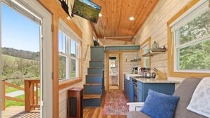 A cabin with a wooden interior, a staircase, a kitchen area, and a view of the outdoors. - Charming Tiny Home! Discounts-Pet friendly (Todd)