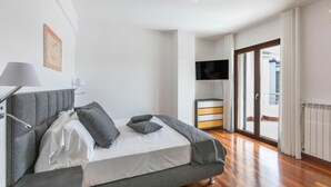 Une chambre moderne avec un canapé-lit gris, un téléviseur à écran plat et une grande fenêtre avec des rideaux.