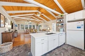 Une cuisine spacieuse avec des meubles blancs, un îlot central et un plafond en bois.