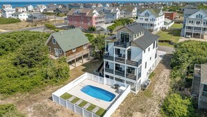 A coastal residential area with a large house featuring a swimming pool, multiple balconies, and a view of the sea. - Wright Off The Beach | 1020 ft to the beach | Private Pool (Kill Devil Hills)