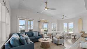 A spacious living room with a blue sofa, a round coffee table, and a dining area with a white table and chairs. - Wright Off The Beach | 1020 ft to the beach | Private Pool (Kill Devil Hills)