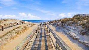 A wooden boardwalk leading to a beach with dunes and a clear sky. - Fancy Free | Oceanfront | Hot Tub (Nags Head)