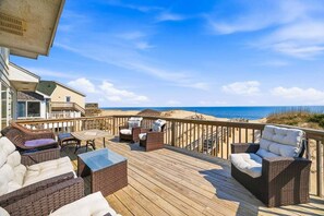A wooden deck with wicker furniture, a table, and a view of the beach. - Fancy Free | Oceanfront | Hot Tub (Nags Head)