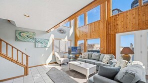 A spacious living room with a large window, a staircase, and a modern fireplace. - Fancy Free | Oceanfront | Hot Tub (Nags Head)
