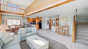 A spacious living area with a high ceiling, a dining area, kitchen, and a staircase leading to an upper level. - Fancy Free | Oceanfront | Hot Tub (Nags Head)