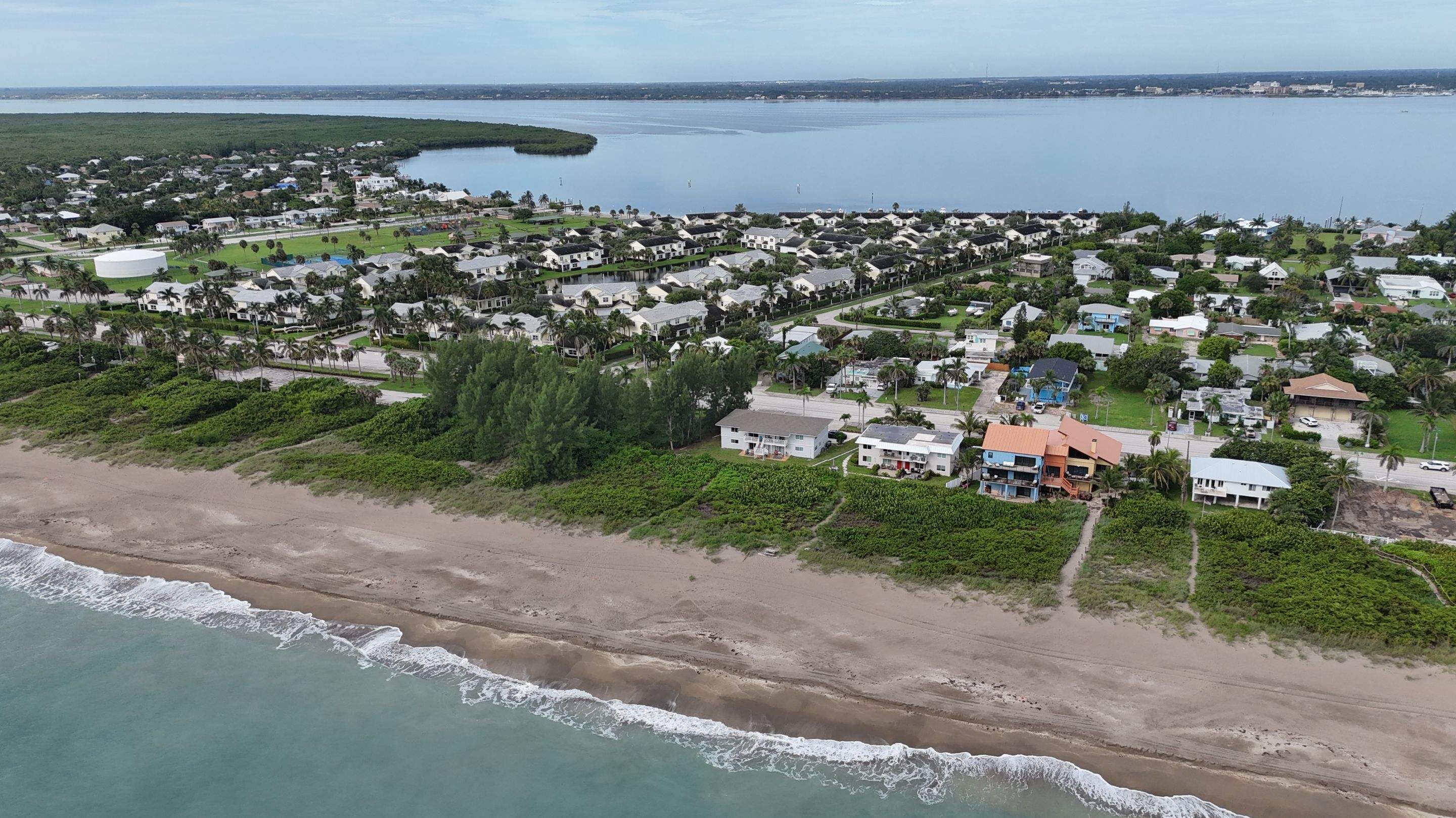 An aerial view of a coastal residential area with houses, a beach, and a large body of water.