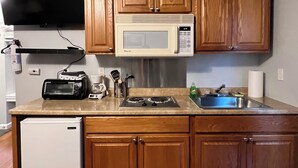 A compact kitchen with wooden cabinets, a microwave, a toaster, and a refrigerator.