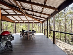 A covered outdoor area with a wooden deck, a table with chairs, and a barbecue grill.