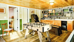 A cozy room with wooden flooring, a foosball table, and a kitchen area with wooden cabinets and a built-in oven. - Winter Bliss at Powderhorn Mountain (Bessemer)