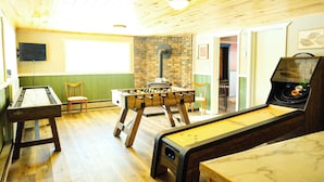 A room with a foosball table, a pool table, and a shuffleboard table. There is a brick wall and a television mounted on the wall. - Winter Bliss at Powderhorn Mountain (Bessemer)