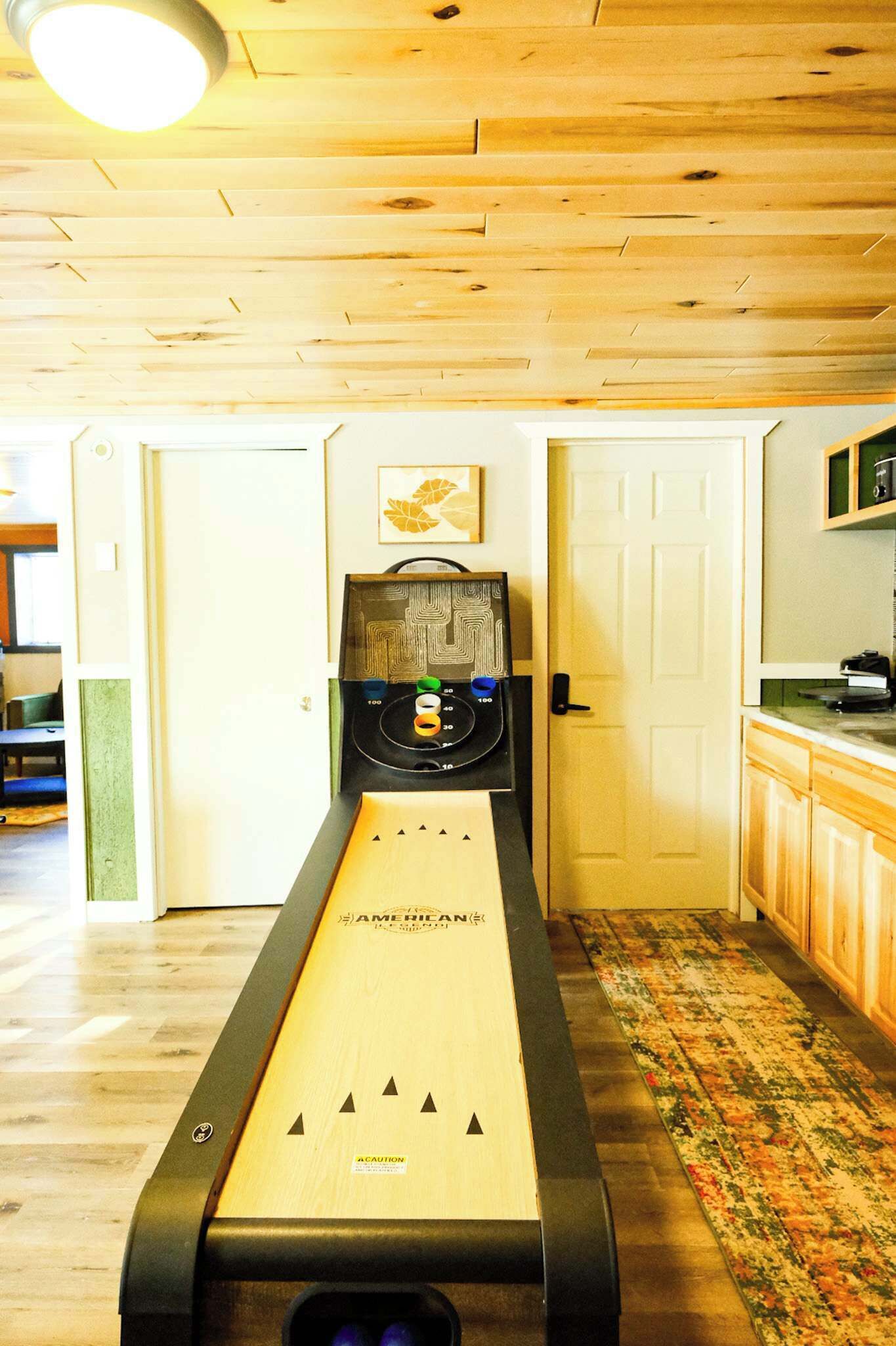 A shuffleboard table in a room with wooden floors and a patterned rug.