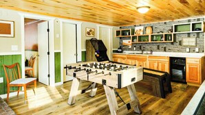 A cozy room with wooden flooring, a foosball table, and a kitchen area with wooden cabinets and a built-in oven. - Elevated Ski Chalet at Powderhorn Mountain (Bessemer)