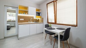Een compacte keuken met witte kastjes, een houten aanrechtblad en een eethoek met twee stoelen en een tafel.