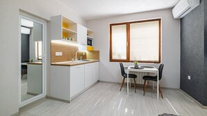 Een kleine keuken met een eethoek, een inbouwoven en een raam met zonwering.