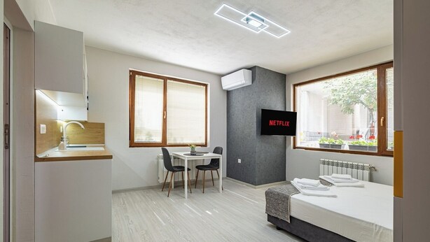 Een moderne, compacte kamer met kitchenette, een eethoek, een bed en een aan de muur bevestigde televisie.