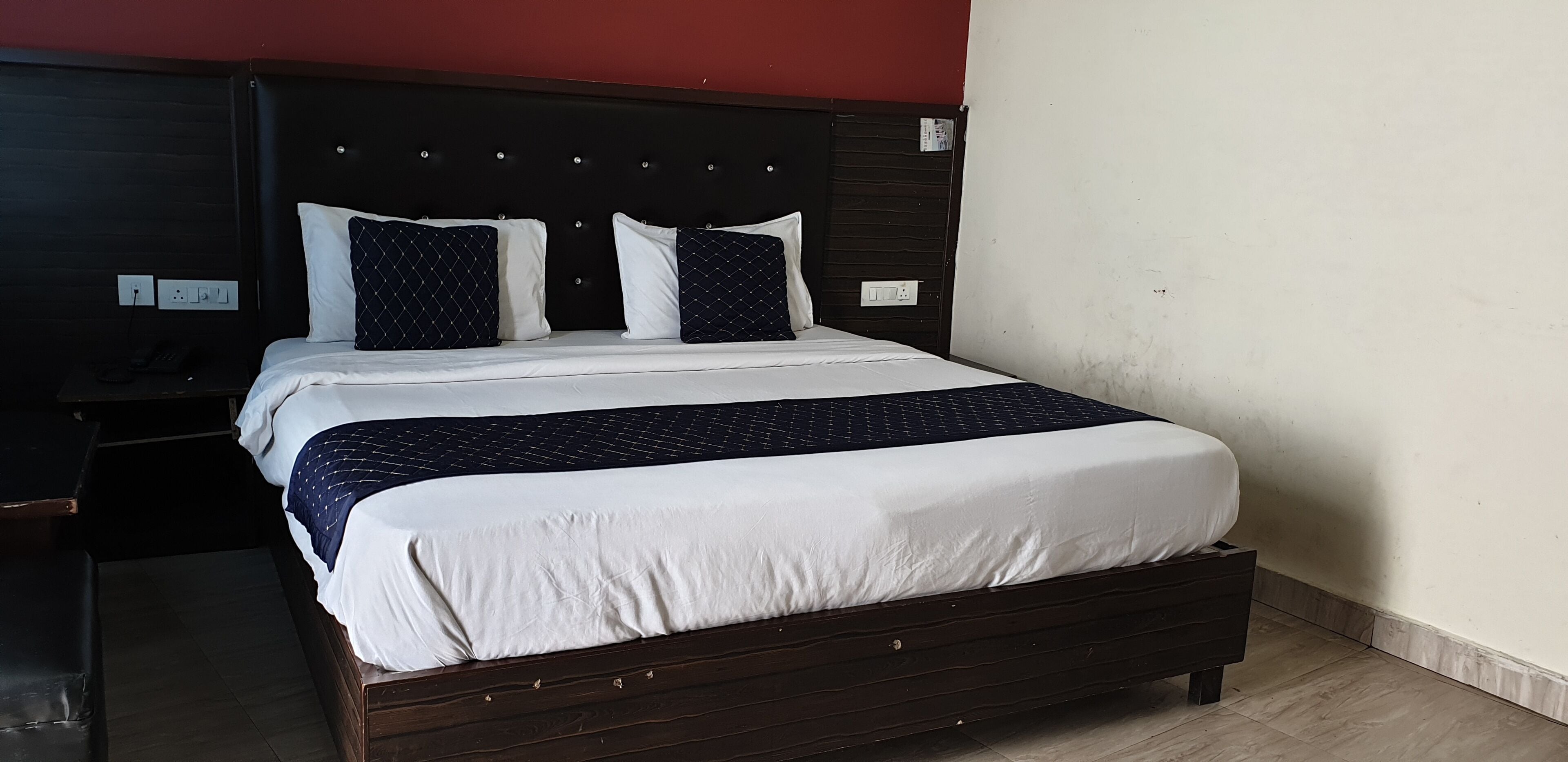 A neatly made bed with white and navy bedding, a dark headboard, and a wooden nightstand with a phone.