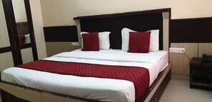 A neatly made bed with white and red bedding, a wooden headboard, and a bedside table with a phone. - Soham Hotel  (Dharamshala)