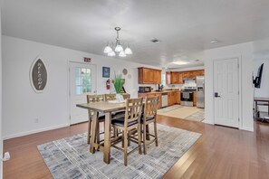 Una cocina moderna con armarios de madera, un comedor con mesa y sillas, y un pasillo que conduce a una salida.