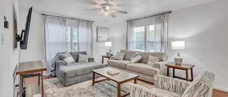A modern living room with a ceiling fan, two sofas, a coffee table, and a striped armchair.