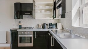 A modern kitchen with black cabinets, a stainless steel sink, a built-in oven, and a microwave. - Luxe Marylebone 2BR, Modern Furniture & Decor, by Blueground (London)