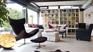 A modern living room with a large bookshelf, a leather pouf, and a dining table. - (WOH15) Holiday home "Kapitänsresidenz" - Holiday home "Kapitänsresidenz" up to 8 persons (Timmendorfer Strand)