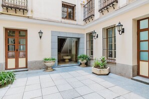 Enter a serene courtyard with lush greenery and a modern entrance.