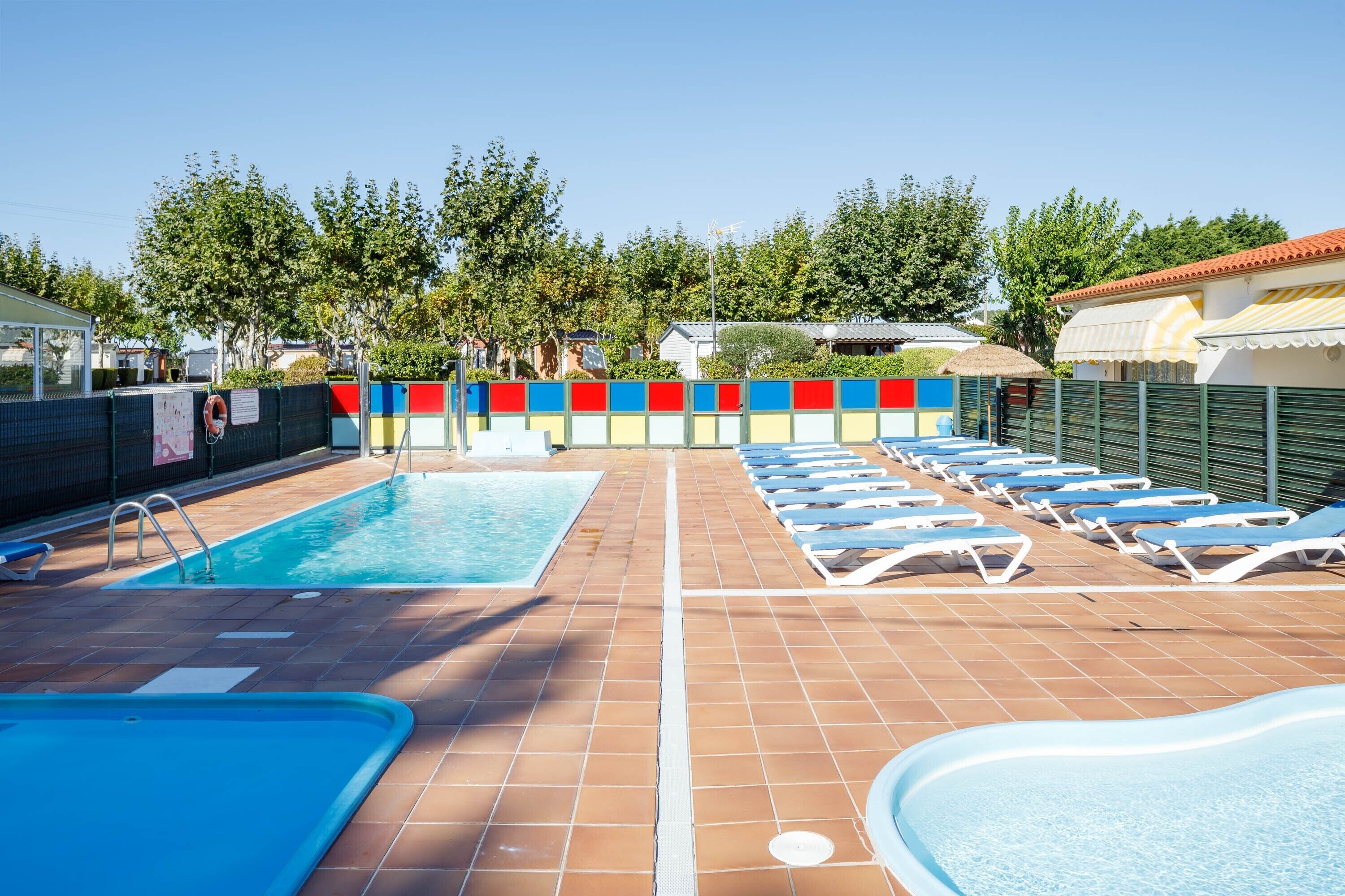 A swimming pool with lounge chairs, a tiled deck, and a colorful fence.