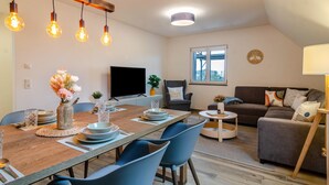 A modern living room with a dining area, a flat-screen TV, a sofa, and a window. - Apartment 'Bergblick' with Shared Terrace, Sauna, Whirlpool & Pool (Stockach)