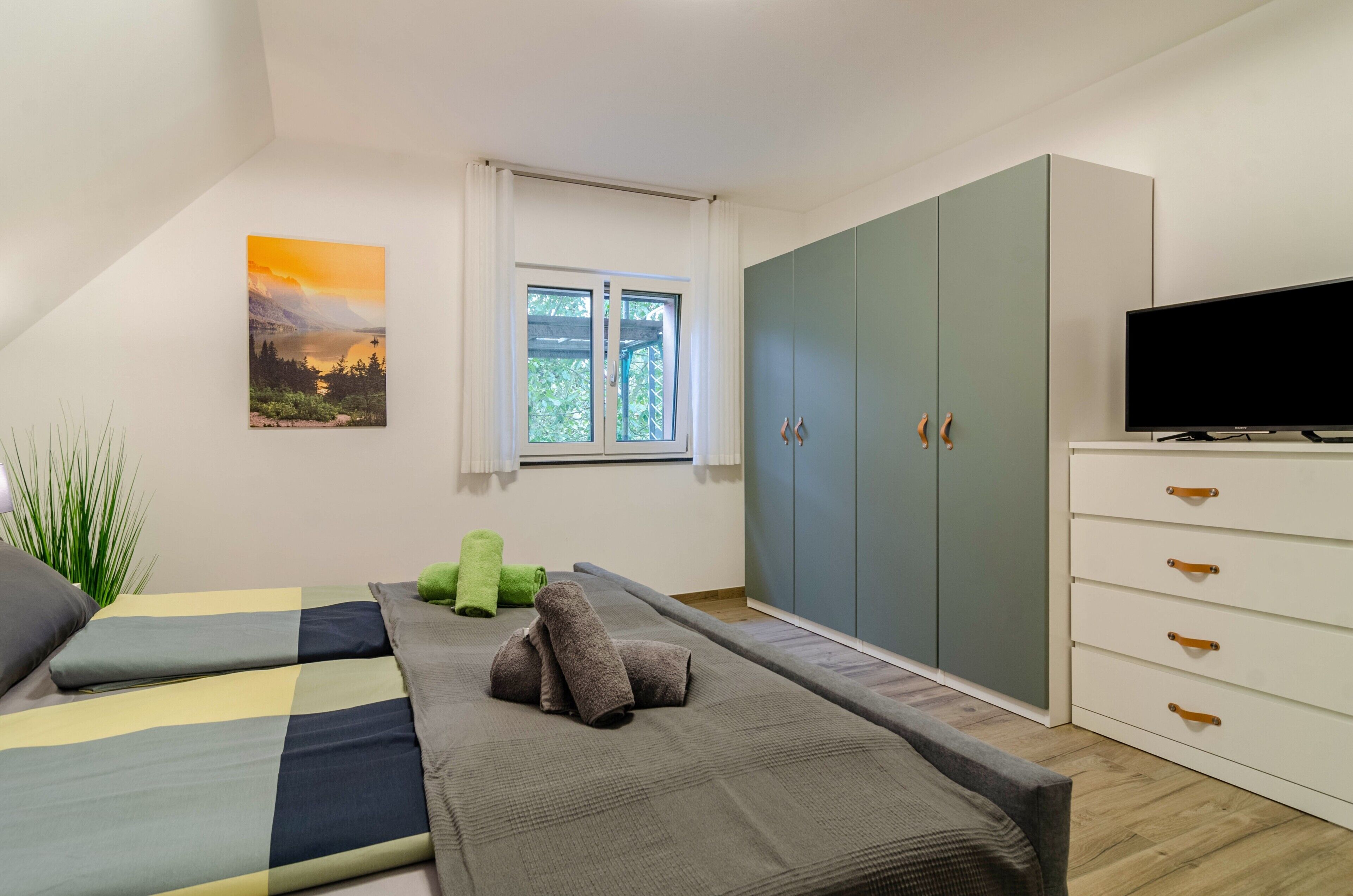 Ein Schlafzimmer mit Bett, Fernseher, Kleiderschrank und einem Fenster mit Vorhängen.