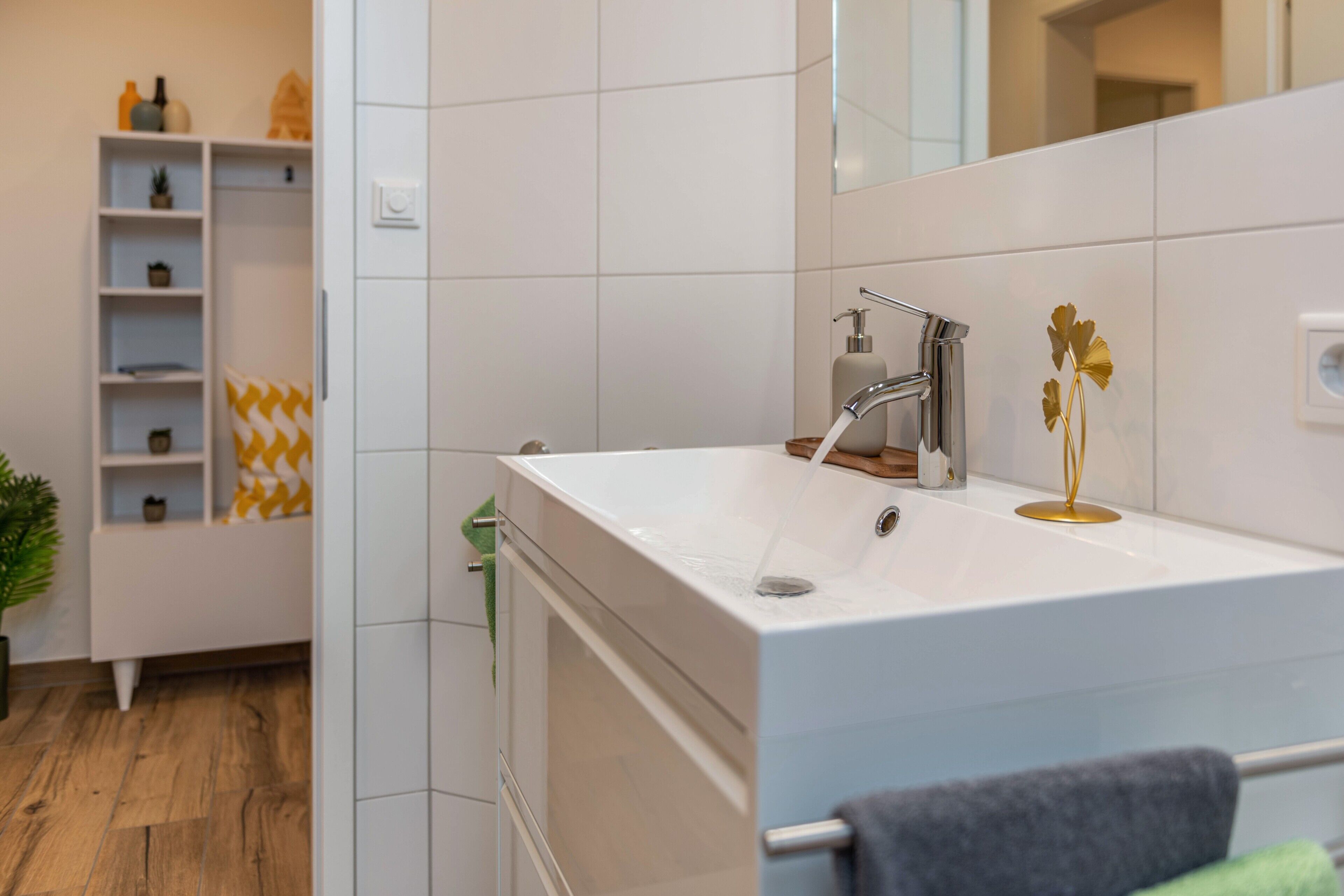Een moderne badkamer met een witte wastafel, een spiegel en een plank met toiletartikelen.