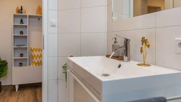 Een moderne badkamer met een witte wastafel, een spiegel en een plank met toiletartikelen.