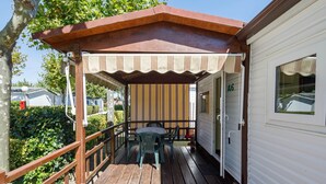 A covered outdoor area with a table and chairs, a wooden railing, and a white building with a window. - Bungalow 'A4' with Private Pool, Private Terrace and Wi-Fi (Pontevedra)