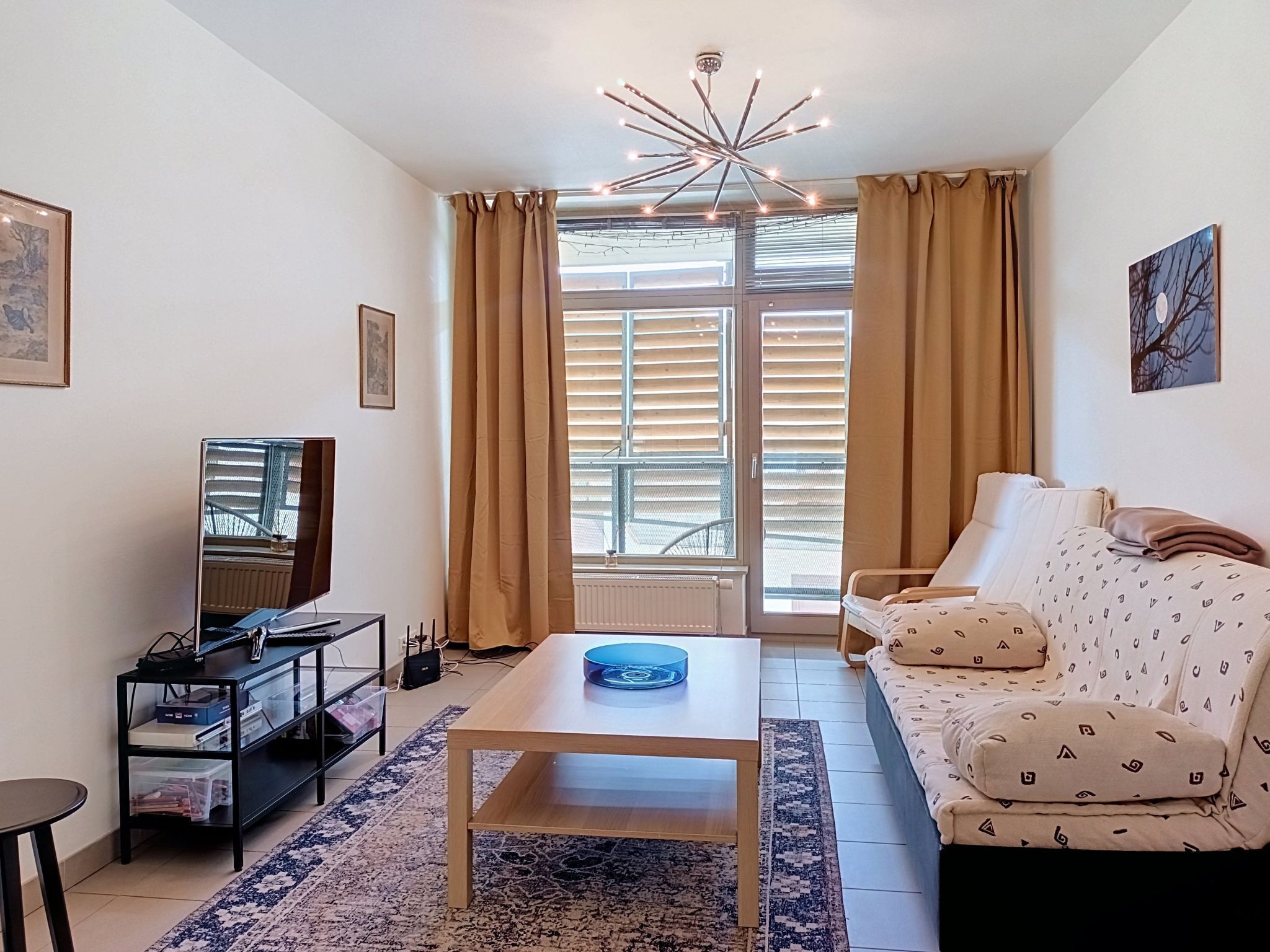 A living room with a sofa, a coffee table, a TV, and a window with curtains.