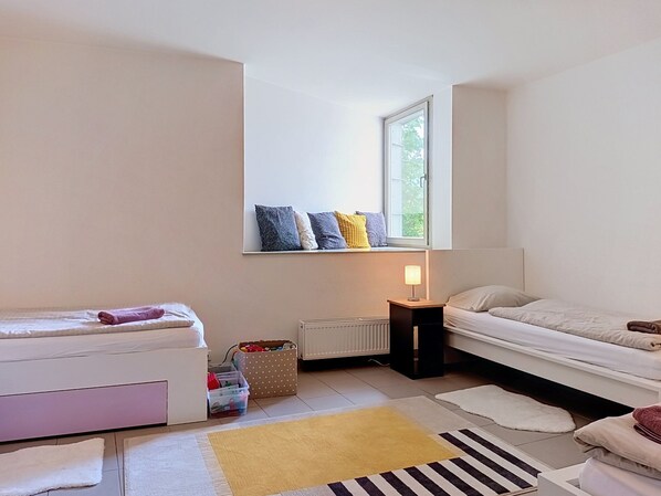 A bedroom with a bed, a window with a view, a bedside table with a lamp, and a small storage unit.