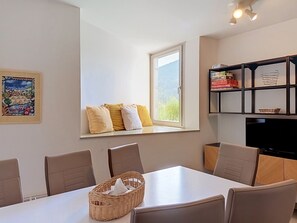 A dining area with a table, chairs, a window with pillows, a bookshelf, and a framed picture on the wall. - Čertovka by Interhome (Harrachov)