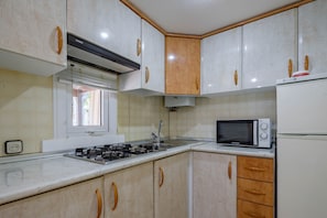 Une cuisine avec des meubles blancs, un four à micro-ondes, un réfrigérateur, une fenêtre et une cuisinière à gaz.