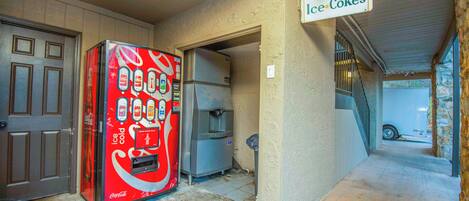 Una máquina expendedora de Coca-Cola frente a un edificio con un letrero que dice 'Ice Cokes'.