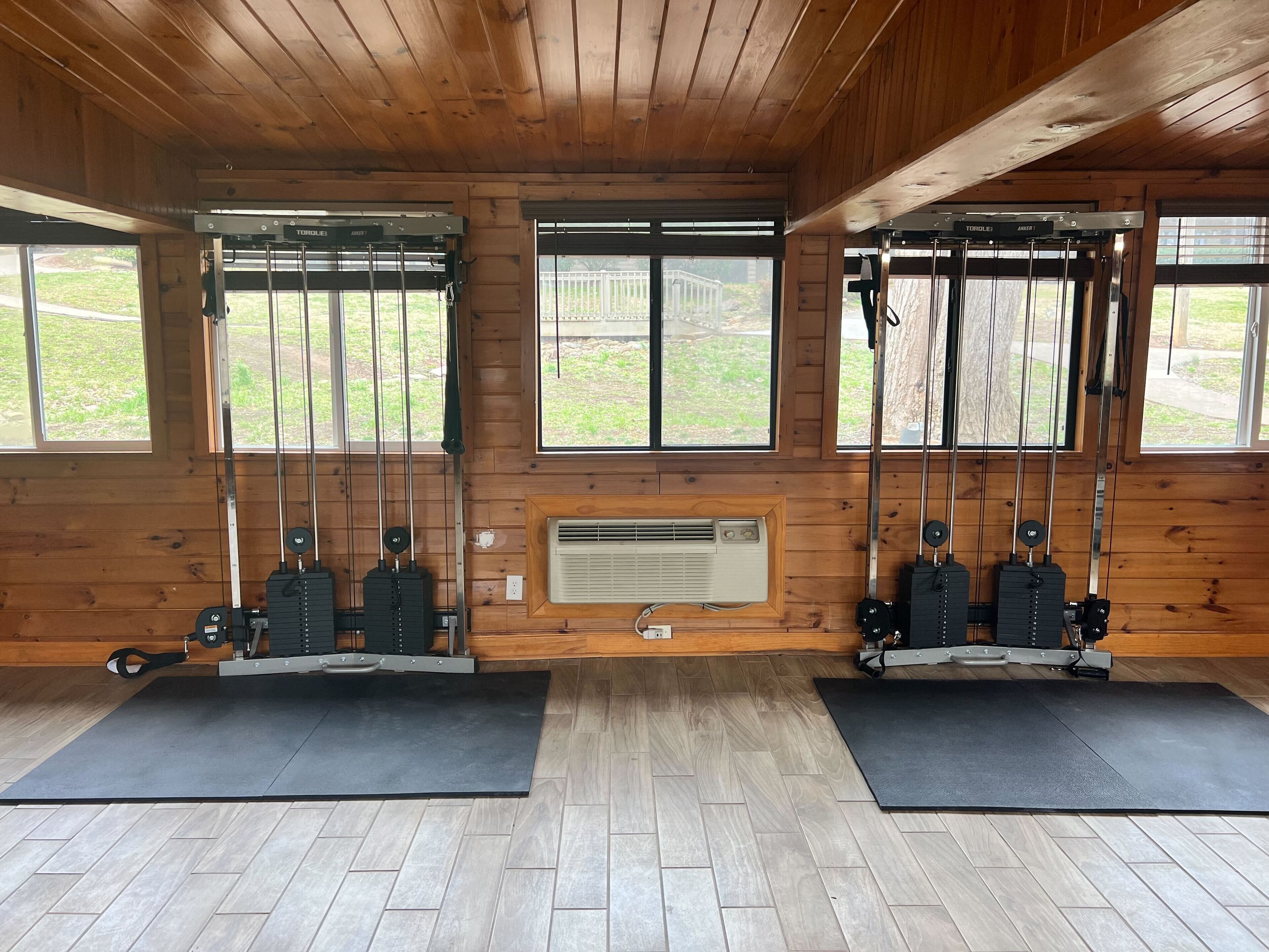 A gym with two pull-up bars, a wall-mounted air conditioner, and large windows.